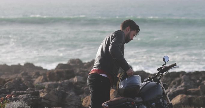 Handsome man wearing leather jacket getting off of classic motorcycle