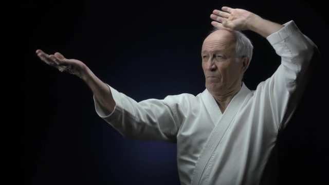 Old male athlete is training formal karate exercises against a dark background