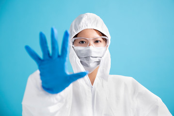 female nurse wearing medical mask with safety glasses and in white protective suit. showing stop and no sign gesture