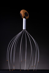 Brightly shining metal of a head massage tool with rounded tips and wooden handle bulb to perform a type of acupressure on the scalp causing stress relieve and a tingling relaxing sensation.