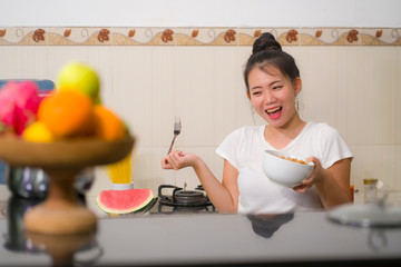 young cute Asian woman eating healthy - beautiful and happy Chinese girl at home kitchen having lunch smiling cheerful holding food bowl in healthy nutrition