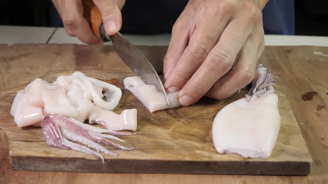 Woman chef cutting squid raw calamari into rings on a wooden cutting board carefully, close up shot