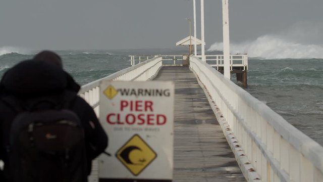 A person watching a pier that has been closed to rough seas.