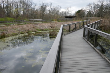 Obraz na płótnie Canvas Wooden foot bridge crossing pond with moody sky reflection in public park