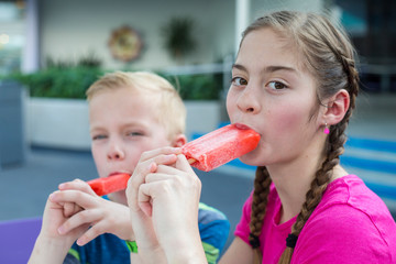 A boy and a girl eating strawberry popsicle ice cream treats on a summer day. Cool treats in the...