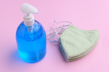 fabric face mask and alcohol gel bottle sanitizer on pink background
