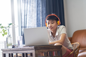 Asian teenage boy studying at home during pandemic wearing headset and smiling
