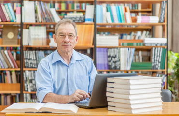 Happy senior man using laptop in library. Empty space for text