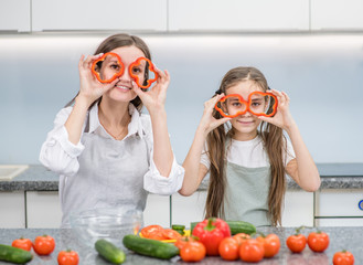 Happy family at home. Mother and young girl preparing healthy food and having fun, holds a pepper in front of their eyes like a glasses