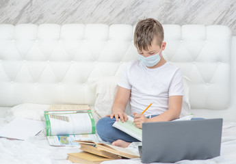 Boy wearing medical protective mask is engaged in distance learning with a laptop. Quarantine and coronavirus epidemic concept. Empty space for text