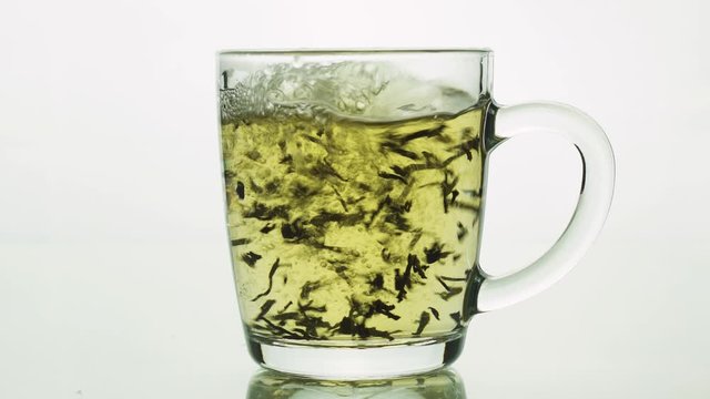 black tea particles pouring into glass transparent mug and filled with boiling water to brew tea isolated on white background close up