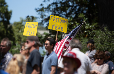 Crowd of people at Freedom Protest Rally during Covid-19 Stay-at-Home orders. Signs read FREEDOM...