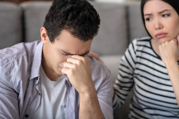 Unhappy guy closing his eyes and worried wife.