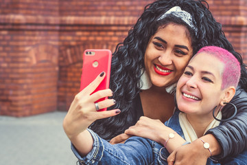 Happy brazilian bright girls take a selfie. Girlfriends have fun outdoors. Friends photographed. Youth lifestyle - obrazy, fototapety, plakaty
