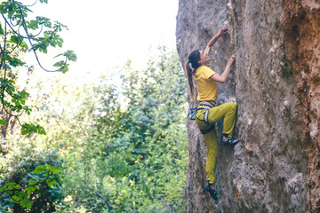 Fototapeta premium A strong woman climbs a rock on the background of the forest.
