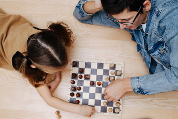 Top view on a father in glasses and his pig-tailed little daughter playing chess