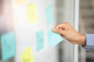close up of asian businessman employee hand using and placing sticky note on glass board arranging...