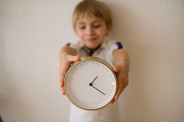  boy, preschool age, against background of white wall, with big clock in his hands. Daylight