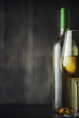 Transparent bottle of white dry wine on the table. White wine glass on a wooden background.