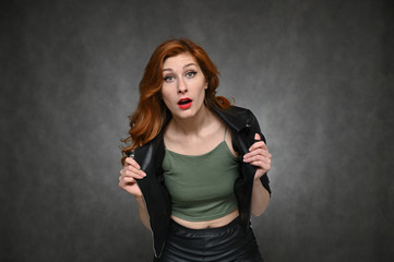 The model demonstrates vivid emotions by changing poses. Portrait of a young pretty woman with beautiful hair and excellent make-up in a green T-shirt and a black jacket on a gray background.