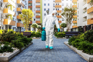 Full length of man in protective sterile suit disinfecting public park from corona virus/ covid-19.