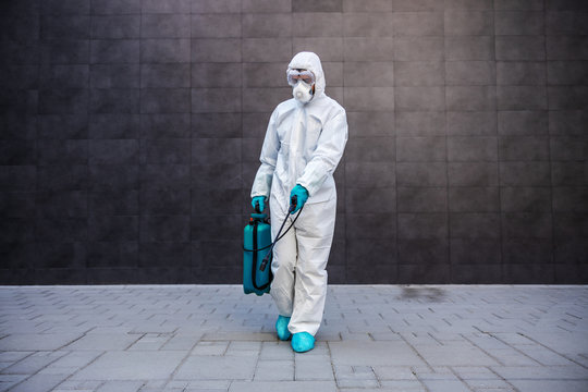 Full length of man in sterile uniform and mask sterilizing surface outdoors from corona virus, fungus and disease.
