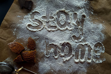The inscription stay home made from white wheat flour. Scattered cookies, nuts, chocolate on a dark background, hand-written flour word Stay home