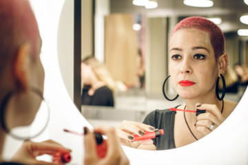 Stylish young woman with short haircut paints her lips with red lipstick near the mirror. Girl with...