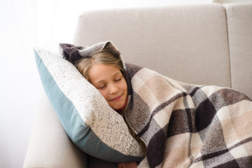  girl lies on sofa and pillow, hiding in cozy blanket, daytime sleep in room