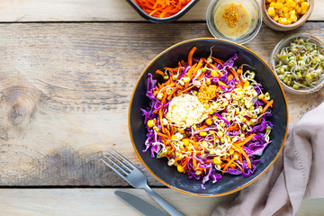 Vegetable salad of fresh red cabbage with carrots, onions, corn, mung seedlings in a plate on wooden background. Selective focus. Top view. Copy space.
