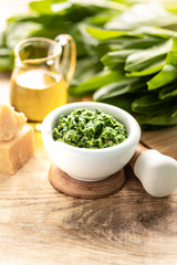 Wild leek pesto with olive oil and parmesan cheese in a white ceramic mortar on a wooden table. Useful properties of ramson.