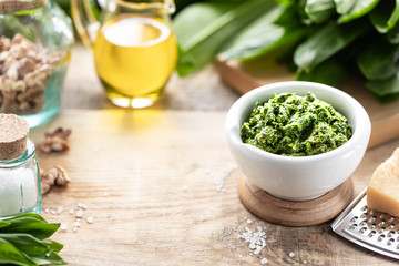 Wild leek pesto with olive oil and parmesan cheese in a white ceramic mortar on a wooden table. Useful properties of ramson. Copy space.