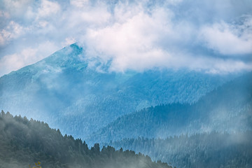 High mountains with green slopes in dense fog. Layers of mountains in the haze during sunset.