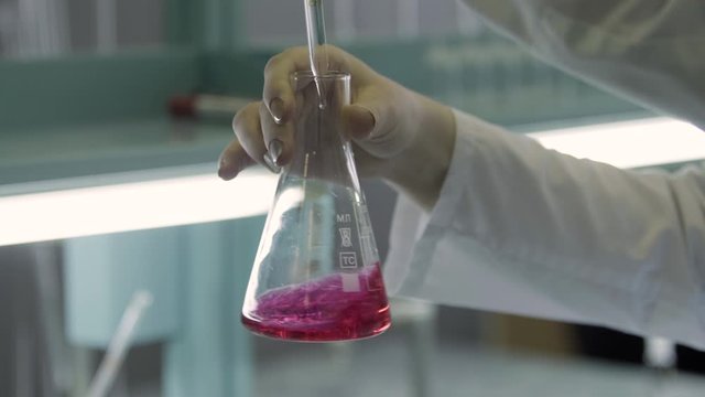 operator adding a drops of transparent solution to a chemical indicator flask and the solution changes colour from purple to yellow close up medical industry