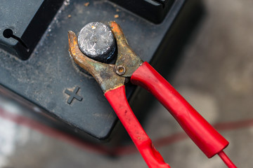 Close up of a car battery with red jumper cable with copper clamps attached to the auto battery.