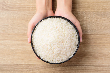 Organic Thai Jasmine rice grain in a bowl holding by hand on wooden background, Top view