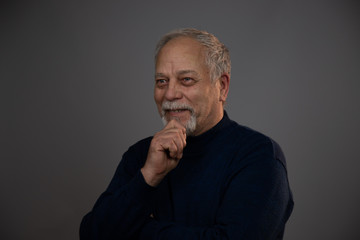 aged man in blue pullover smiles cheerfully holding hand on grey beard close view. Concept man emotion
