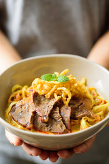 Northern Thai food (Khao Soi), spicy curry noodles soup with coconut milk and beef in a bowl holding by hand