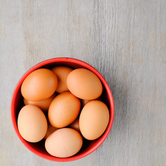 Close-up top view of organic raw eggs in red egg bowl on rustic wooden background with copy space for your text, healthy eating concept.