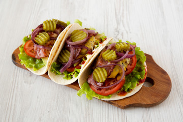 Homemade Bacon Cheeseburger Tacos on a rustic wooden board on a white wooden background, side view.