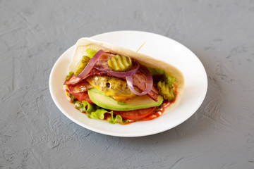 Homemade Bacon Cheeseburger Taco on a white plate on a gray background, side view.