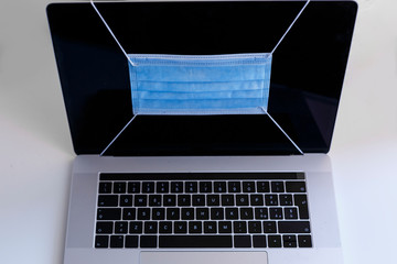 notebook con mascherina chirurgica protettiva nello schermo, sopra un tavolo bianco