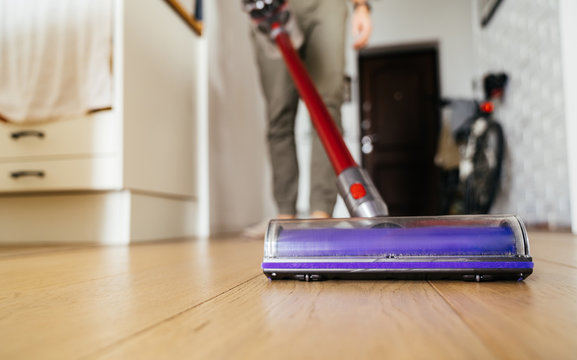 Vacuum cleaner in the hands of man. Cleaning the wooden floor in the apartment.