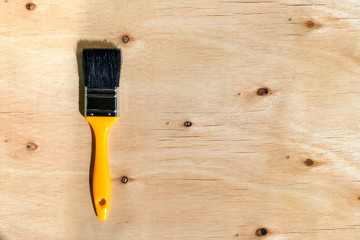 Yellow plastic paint brush with black bristles against light brown wooden background with texture...