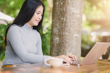 Young woman sitting in coffee shop at wooden table, drinking coffee and using laptop.