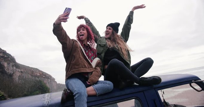 Women sitting on top of van taking selfie with smartphone