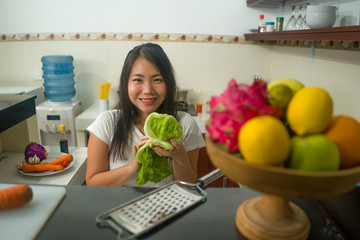 vegetable food and diet - home lifestyle portrait of young beautiful and happy Asian Chinese woman at domestic kitchen smiling cheerful in healthy nutrition and dieting concept