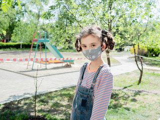 A little girl in a medical mask is not allowed to play in the playground during the coronavirus pandemic.