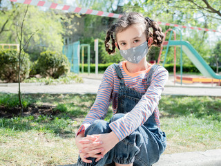 Sad little girl on the background of the closed Playground in the period of quarantine due to coronavirus infection.