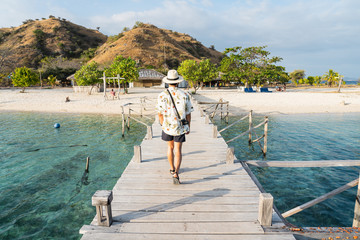 Young man with camera walking on wooden bridge to Kanawa island, Flores island in Komodo national park in Indonesia